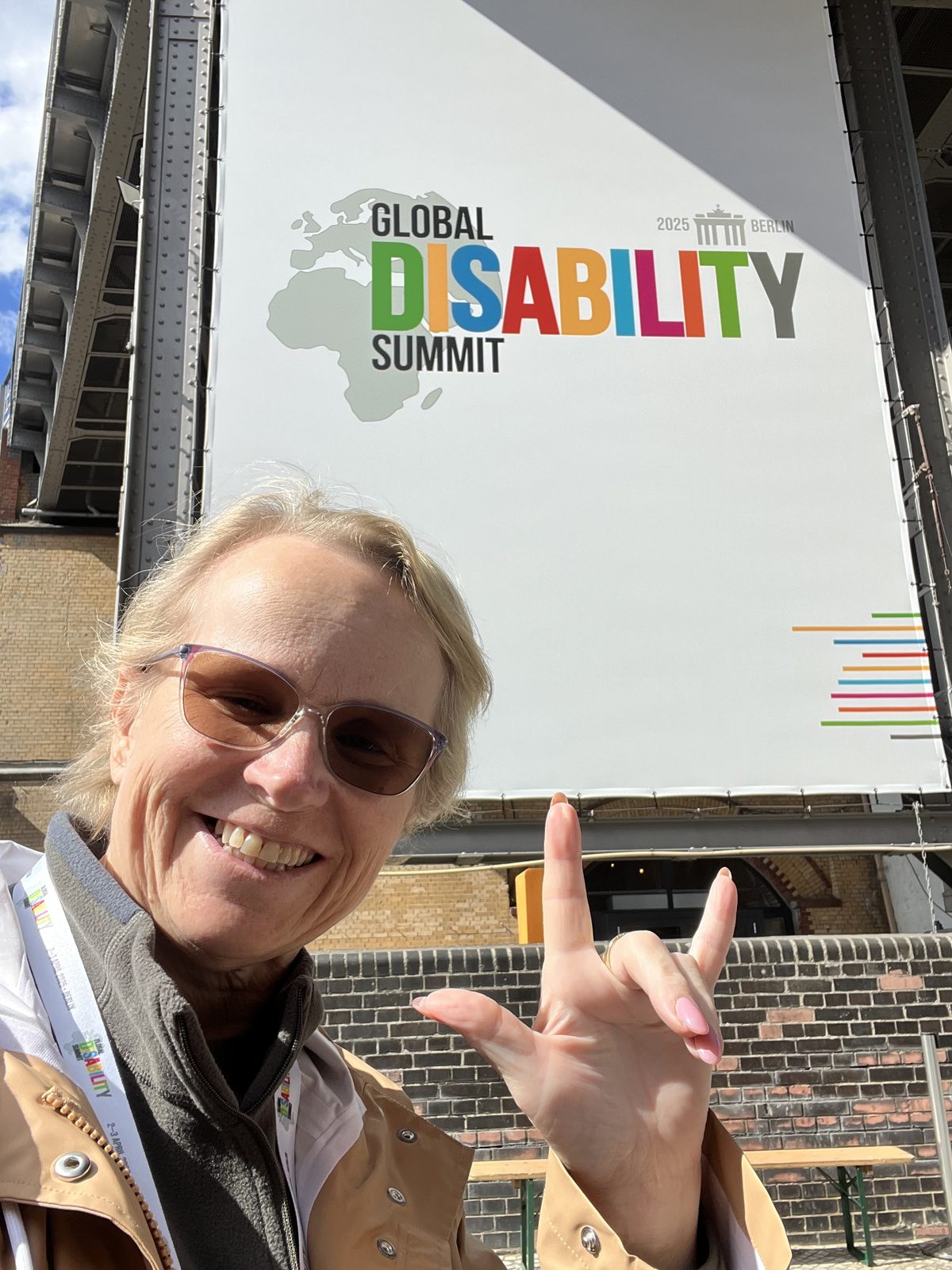 Jody smiling and signing in front of a Global Disability Summit banner
